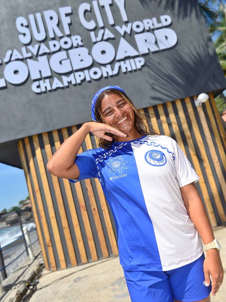 Surfista posando alegremente frente al letrero oficial del ISA World Longboard Championship en Surf City El Salvador.