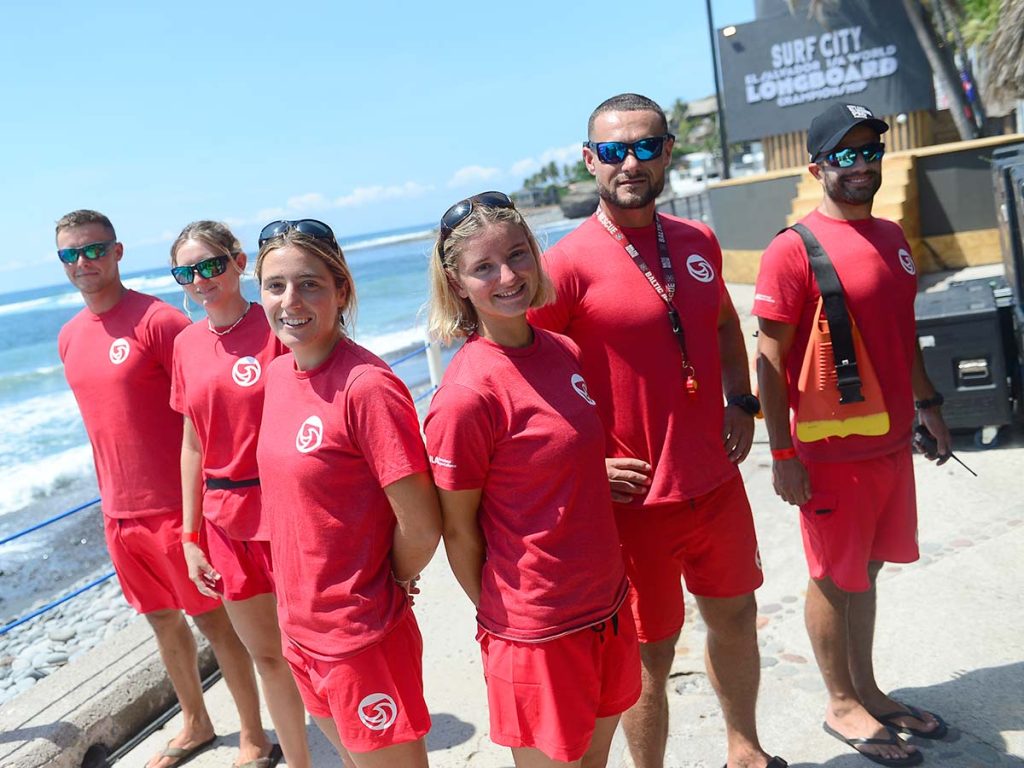 Equipo de salvavidas y socorristas uniformados de rojo posando cerca del mar en el evento mundial de surf.