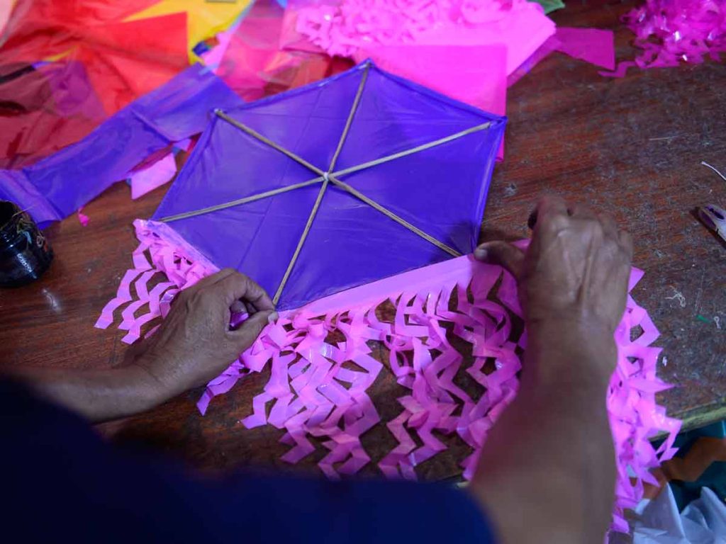 Mano sosteniendo una serie de tiras de plástico con cortes en zigzag en tonos celeste, magenta y anaranjado