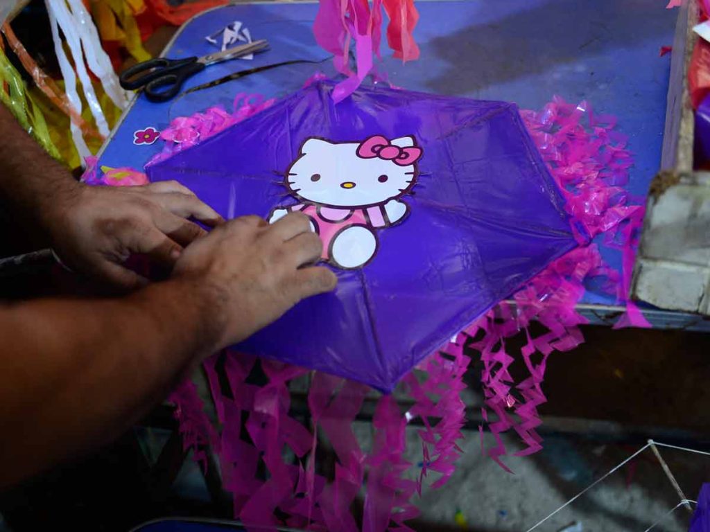 Manos pegando un sticker de Hello Kitty en el centro de una piscucha morada con flecos rosados.