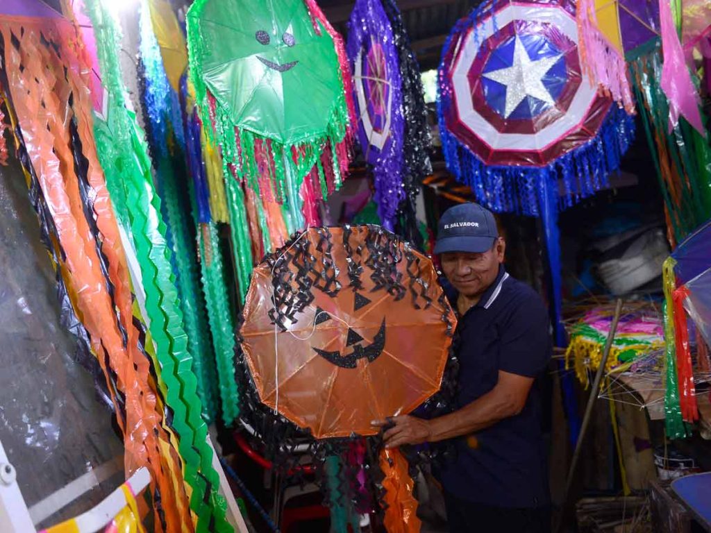 Don Ramiro Peinado sostiene una piscucha circular anaranjada con cara de calabaza de Halloween rodeado de cometas.