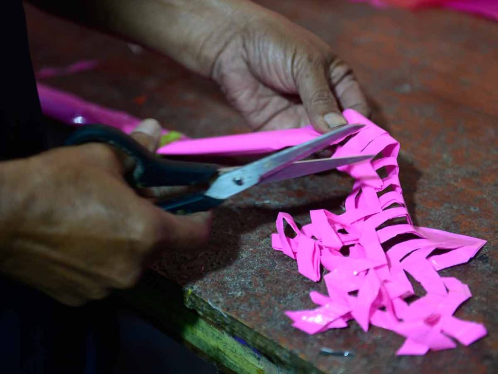 Manos de don Ramiro utilizando tijeras para cortar cuidadosamente los bordes en forma de picos a un pliego de plástico rosado