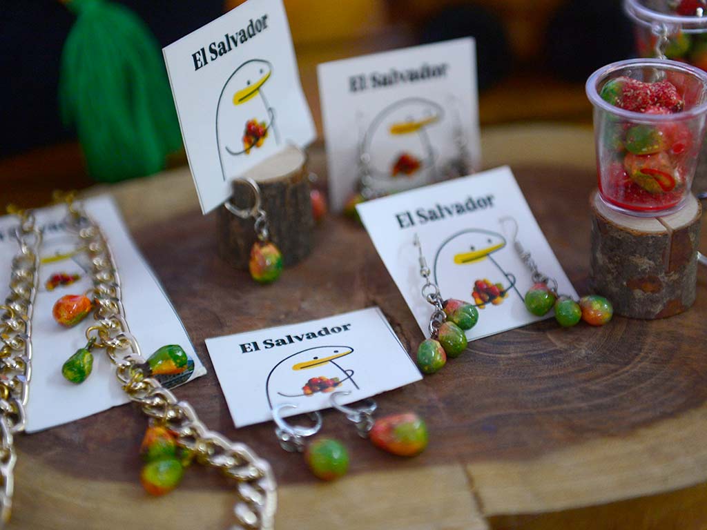 Aretes y collares artesanales en forma de pequeños jocotes exhibidos sobre bases de madera en una feria.