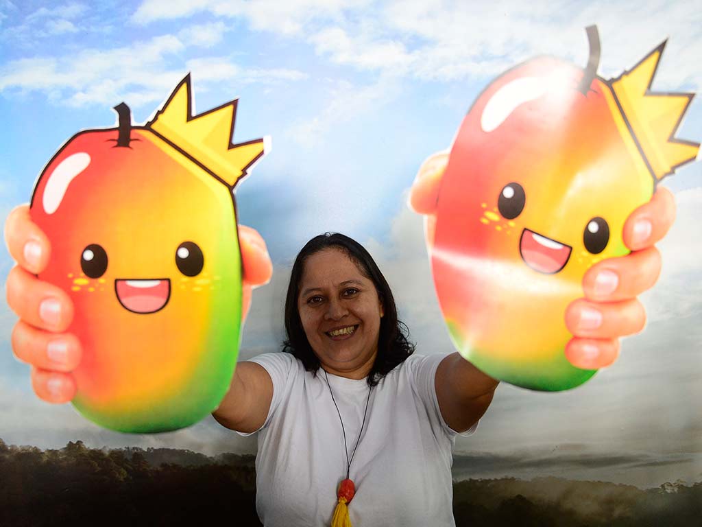 Mujer sonriente mostrando dos ilustraciones coloridas de jocotes coronados.