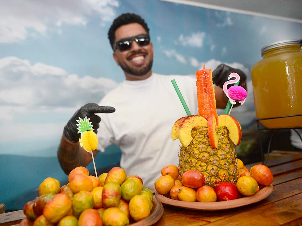 Hombre sonriente mostrando una preparación tropical en piña rodeada de jocotes frescos de corona.