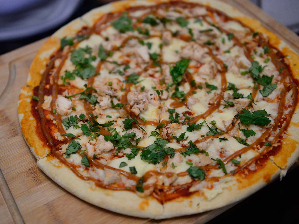 Pizza recién horneada aderezada con salsa especial de jocote y cilantro fresco sobre tabla de madera.