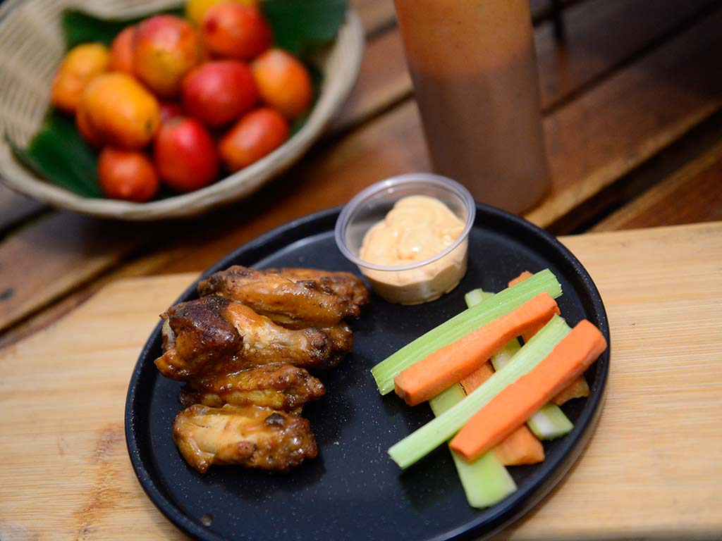 Plato de alitas de pollo aderezadas con salsa de jocote servidas junto a bastones de zanahoria y apio.