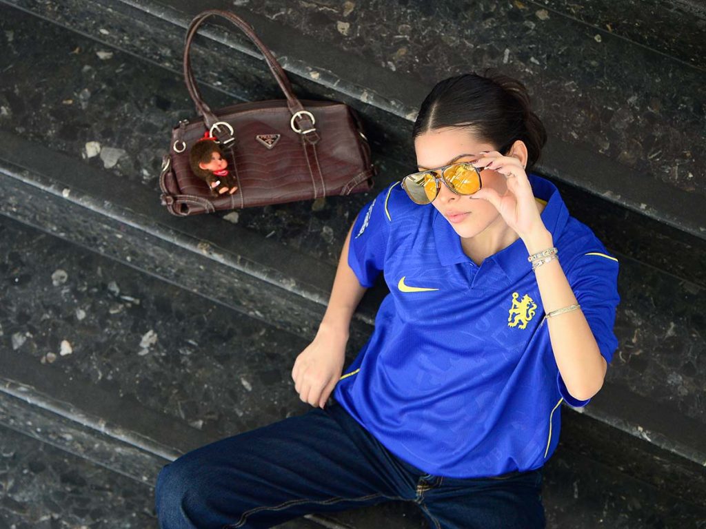 Plano cenital de Gabriela Triste sosteniendo el marco de sus gafas amarillas sentada en escalones.
