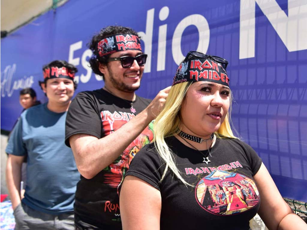 Un hombre ajustando la pañoleta de Iron Maiden en la cabeza de una mujer rubia vestida de negro.