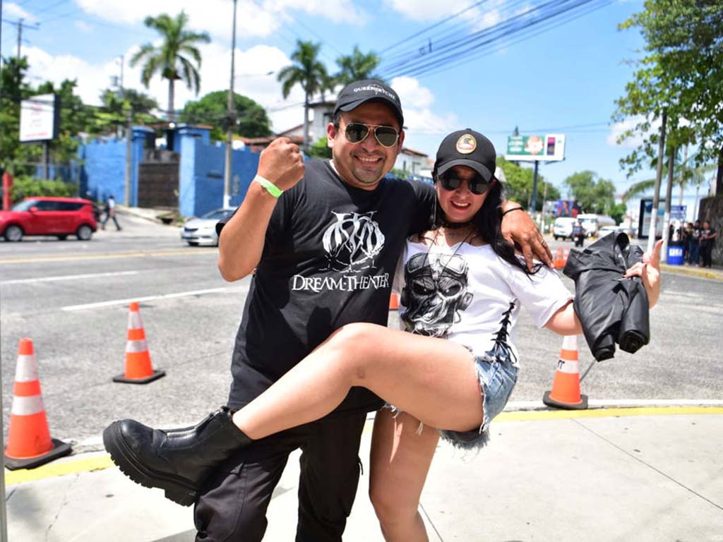 Hombre sosteniendo alegremente en brazos a su pareja que posa levantando la pierna cerca de conos de tránsito.
