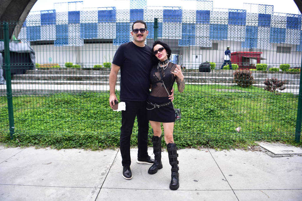 Pareja vestida con ropa oscura y botas góticas posando junto al enrejado del Estadio Jorge Mágico González.
