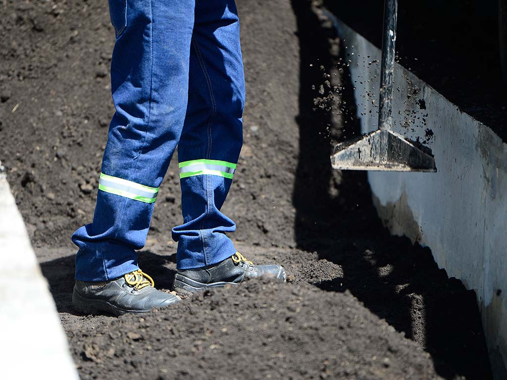 Detalle de un trabajador compactando la tierra negra en el arriate central de la avenida Jerusalén.