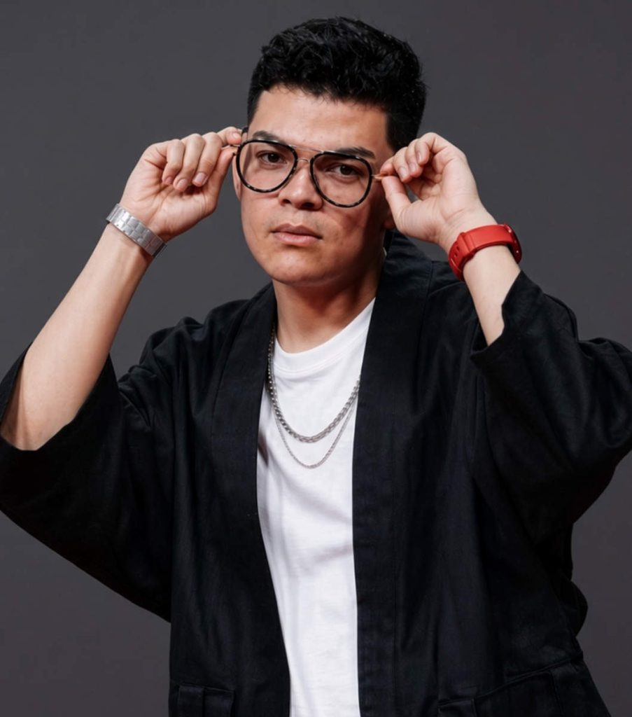 Retrato del streamer salvadoreño El Komanche vistiendo kimono negro, camiseta blanca y lentes de marco oscuro.