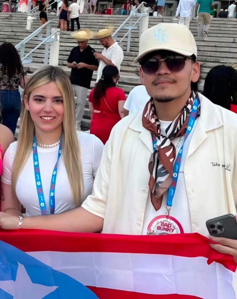 El Komanche vistiendo gorra blanca, lentes de sol y pañuelo al cuello sosteniendo la bandera de El Salvador.