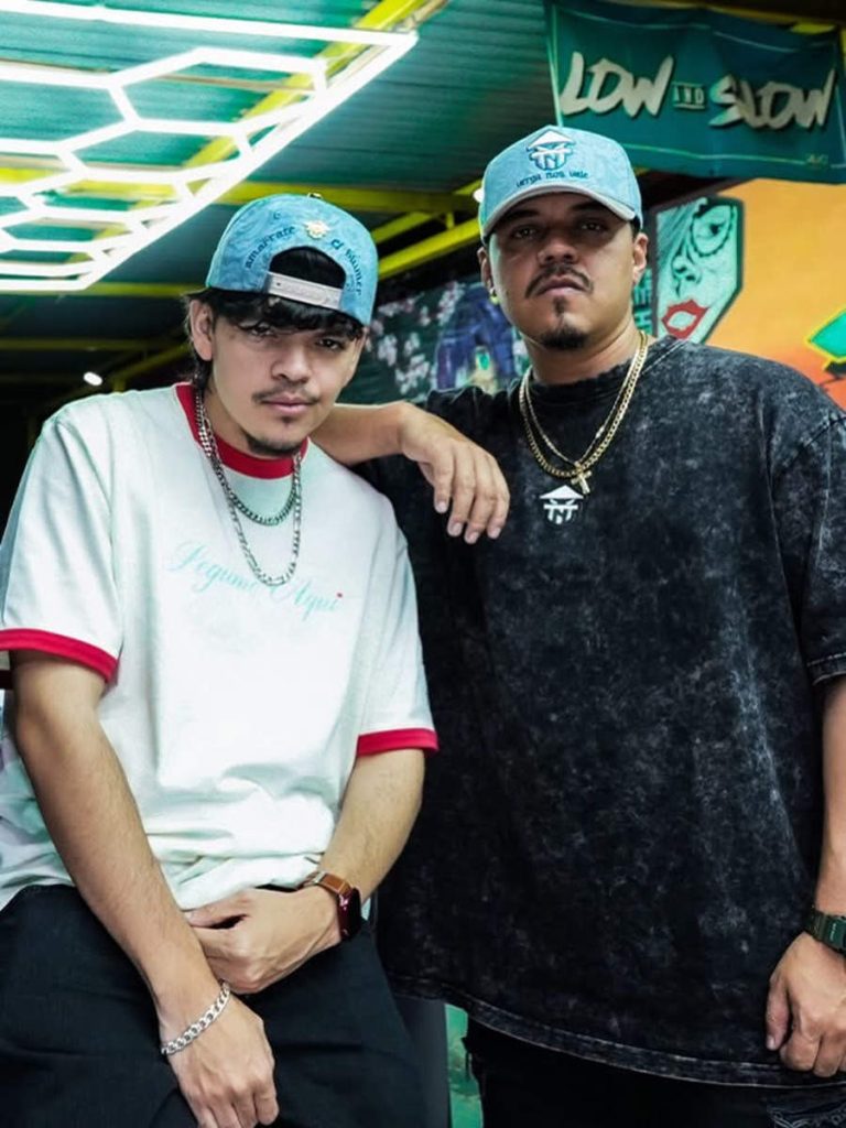 El Komanche con gorra celeste posando junto a otro creador de contenido en una barbería.