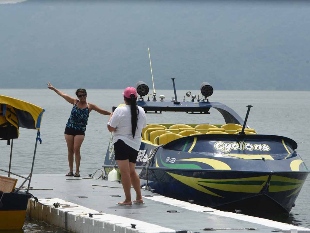 Turistas posando junto a una lancha rápida Cyclone en el embarcadero del Lago de Ilopango