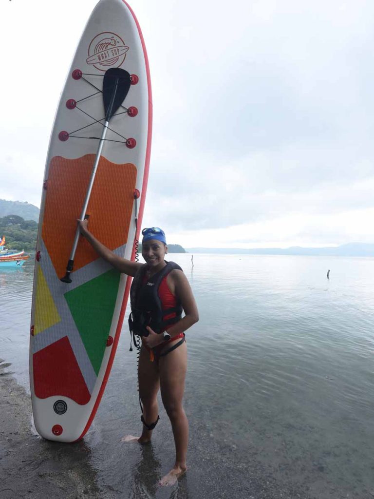 Turista posando junto a su tabla de paddleboard a la orilla del Lago de Ilopango