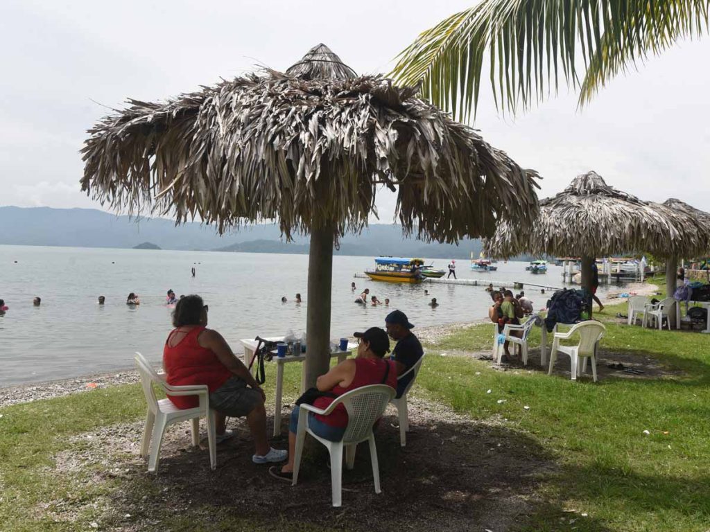 Familias descansando bajo sombrillas de paja frente al Lago de Ilopango El Salvador