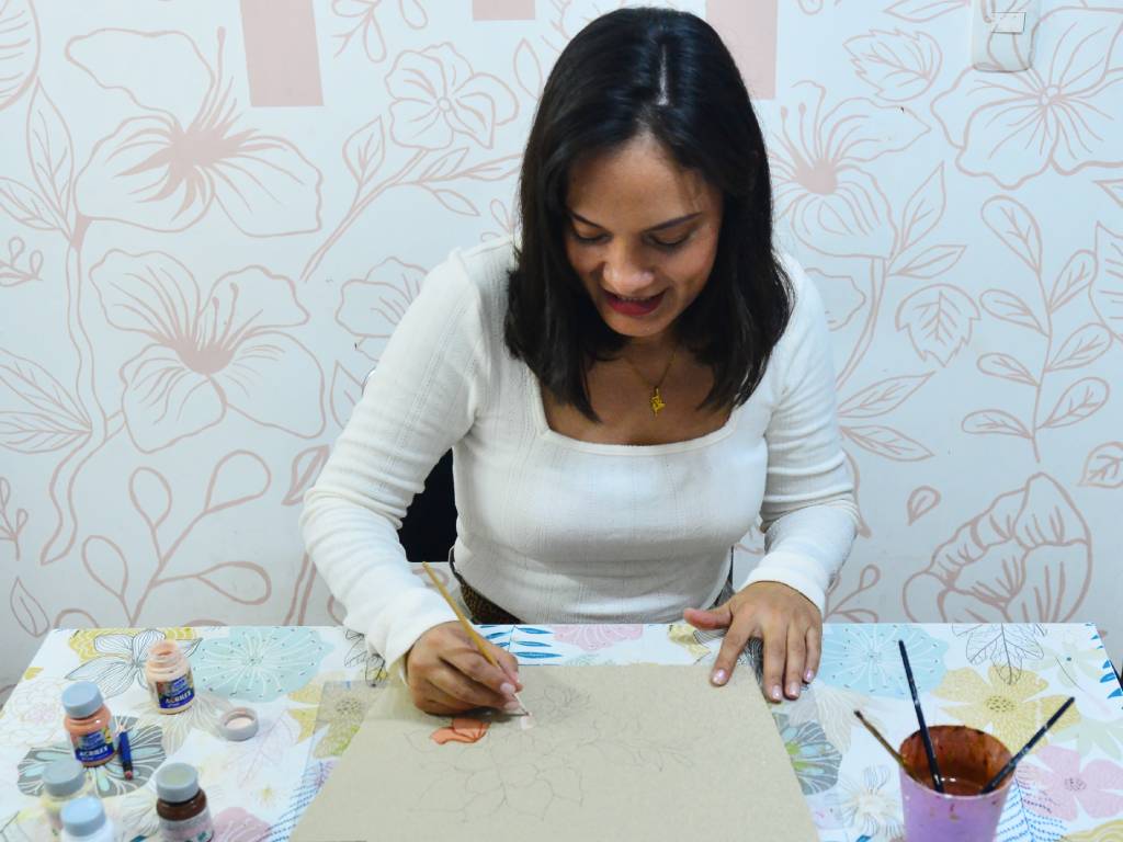 Erika Herrera aplicando pintura de vivos colores sobre la tela trazada para dar vida al diseño de una cartera artesanal.