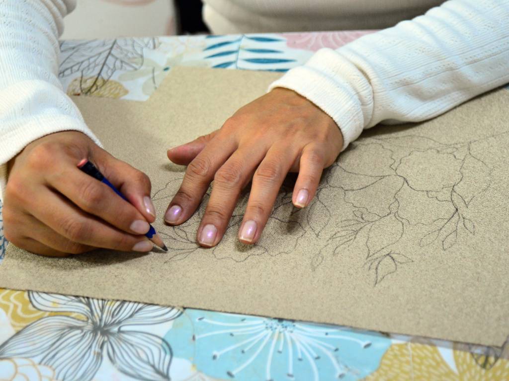 Erika Herrera dibuja a mano sobre una pieza de tela los trazos y el diseño para confeccionar una nueva cartera.