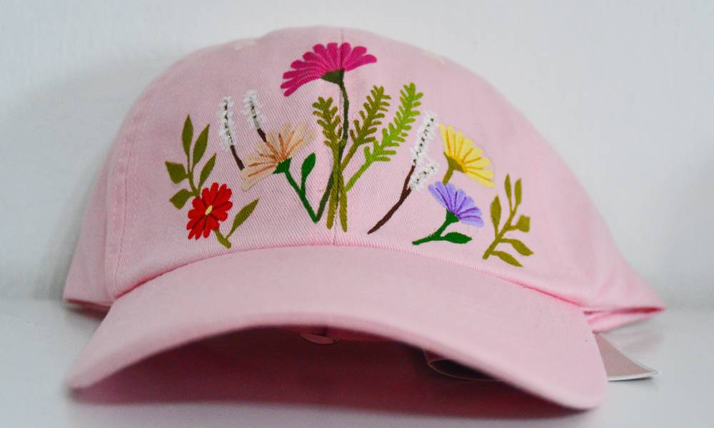 Muestra de gorras artesanales confeccionadas con diseños y telas pintadas a mano junto a la línea clásica de carteras.