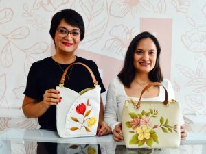 Nancy y Erika Herrera sonrientes junto a la máquina de coser de su madre en el taller familiar ubicado en Sonsonate.