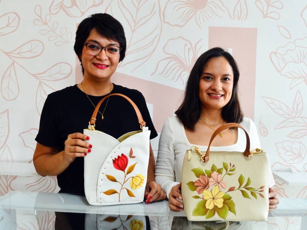 Nancy y Erika Herrera sonrientes junto a la máquina de coser de su madre en el taller familiar ubicado en Sonsonate.