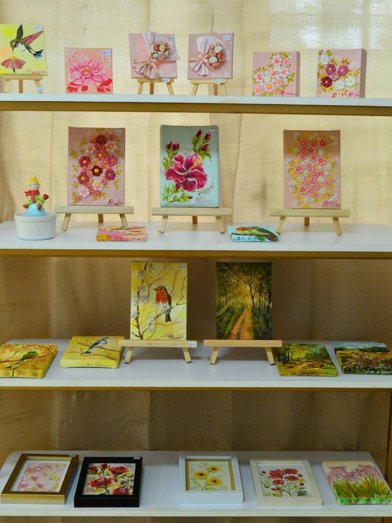 Colección de piezas de arte utilitario como camisetas, joyeros, cofres y accesorios artesanales exhibidos en la galería.