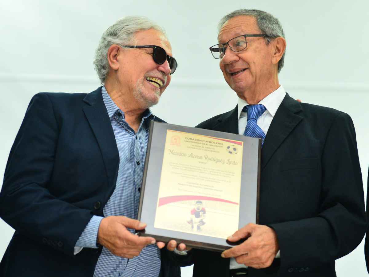 Mauricio «Pipo» Rodríguez sonríe al recibir una placa de reconocimiento de manos de Celso Jurado durante el evento en la UES.