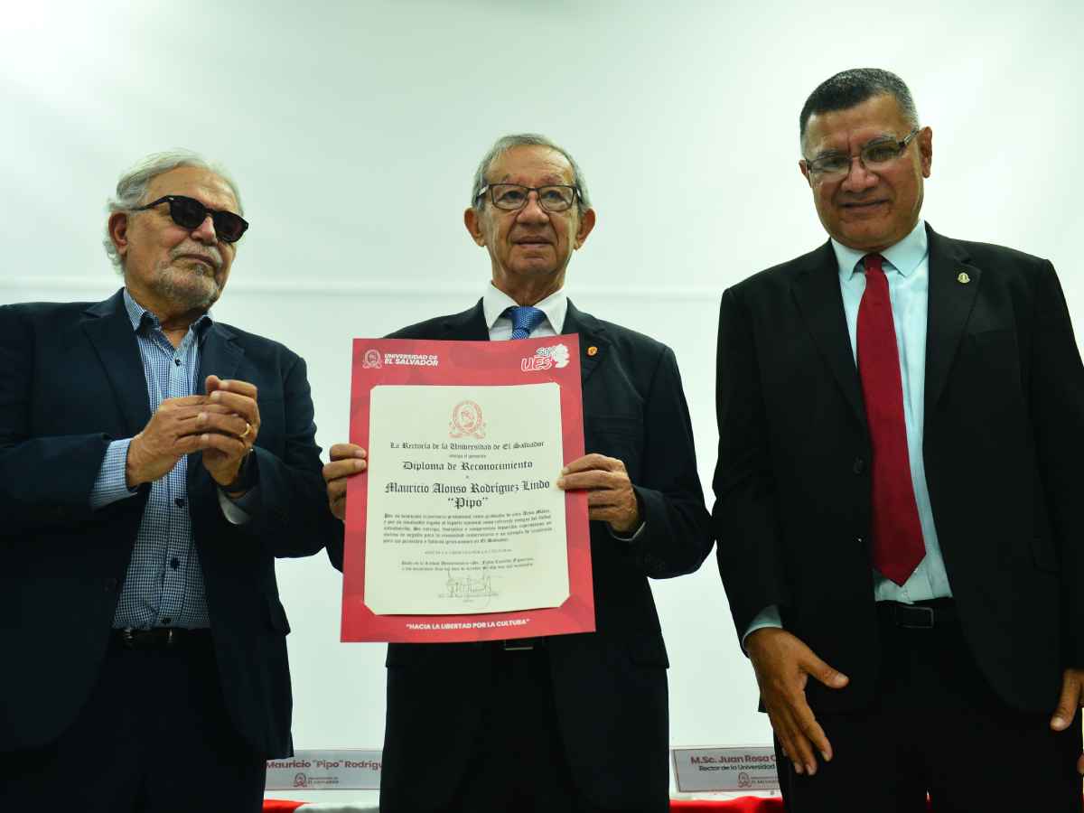 Mauricio «Pipo» Rodríguez recibe con sonrisa un diploma de reconocimiento de manos del rector de la UES, Juan Rosa Quintanilla.