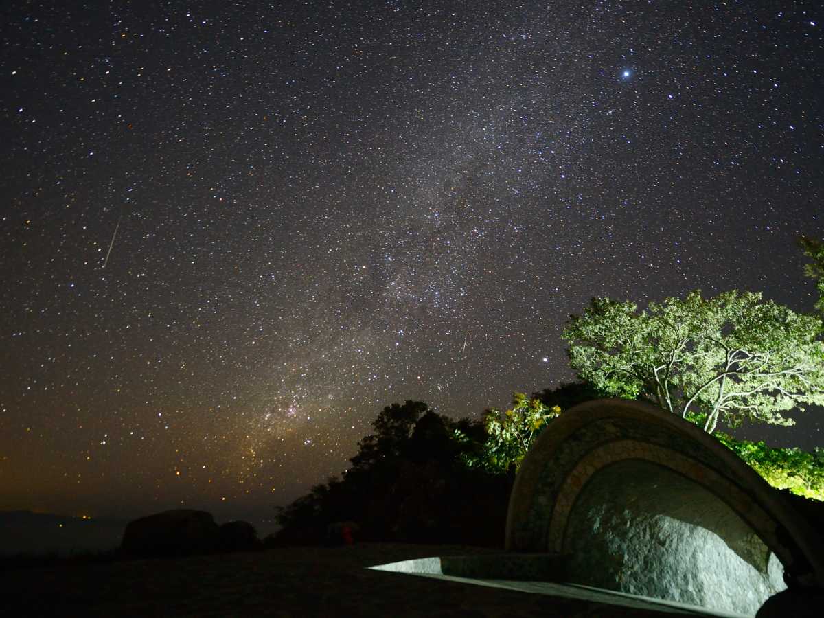 Meteoros cruzando el cielo nocturno con destellos reflejados sobre la superficie oscura del océano.