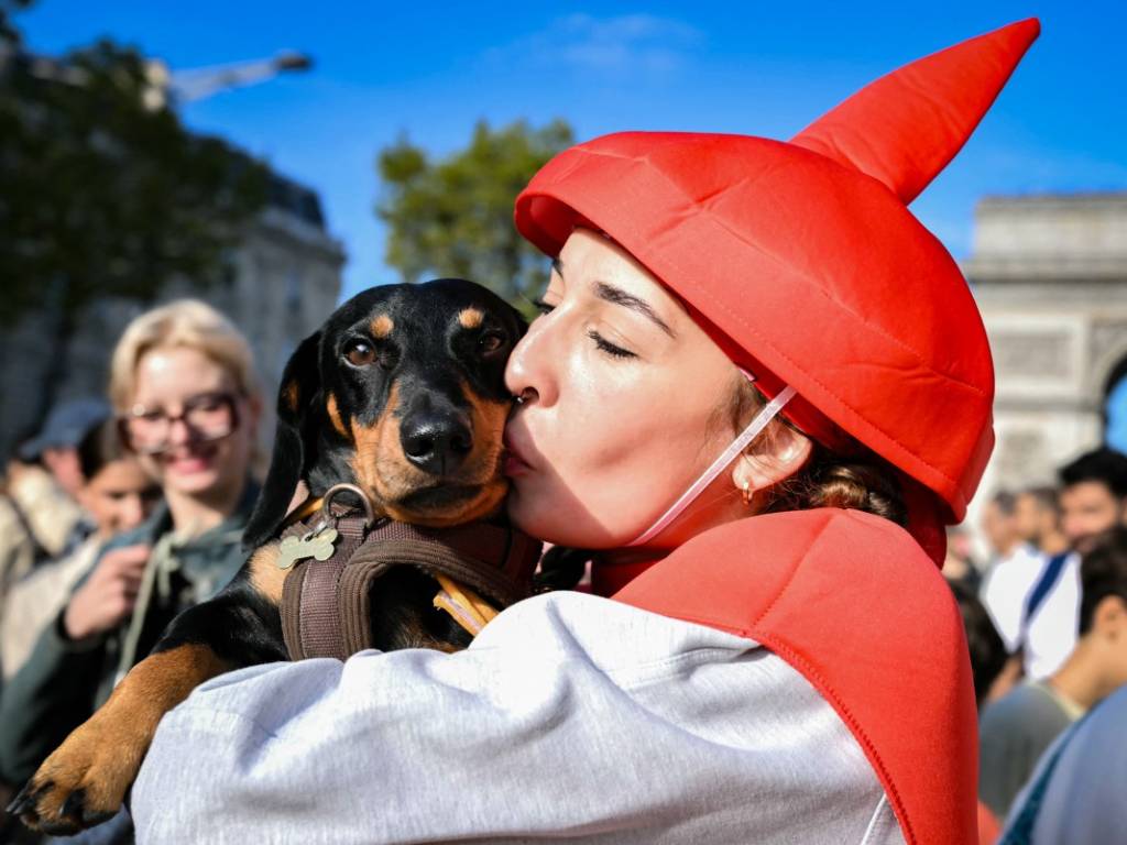 Una mujer sostiene en brazos a su perro salchicha vestido con un disfraz y le da un beso cariñoso durante la marcha.