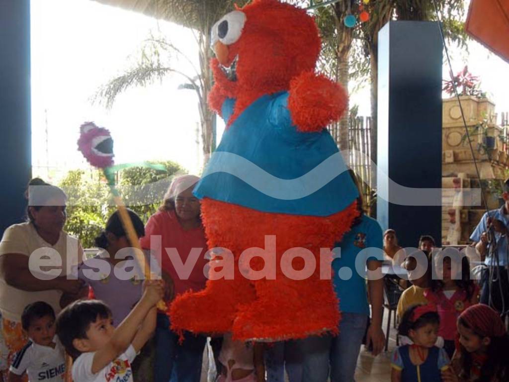 Niños celebrando alrededor de un pastel en una fiesta de cumpleaños decorada dentro del parque de diversiones.