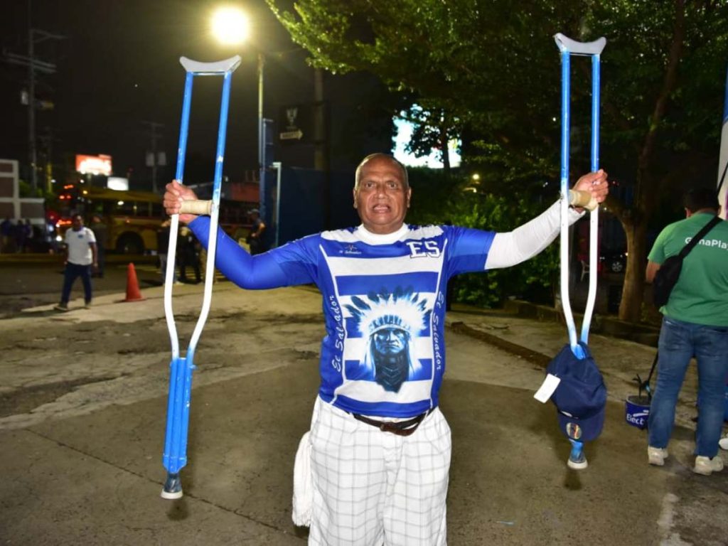Un aficionado posa con sus muletas decoradas de azul y blanco en los alrededores del estadio Cuscatlán.
