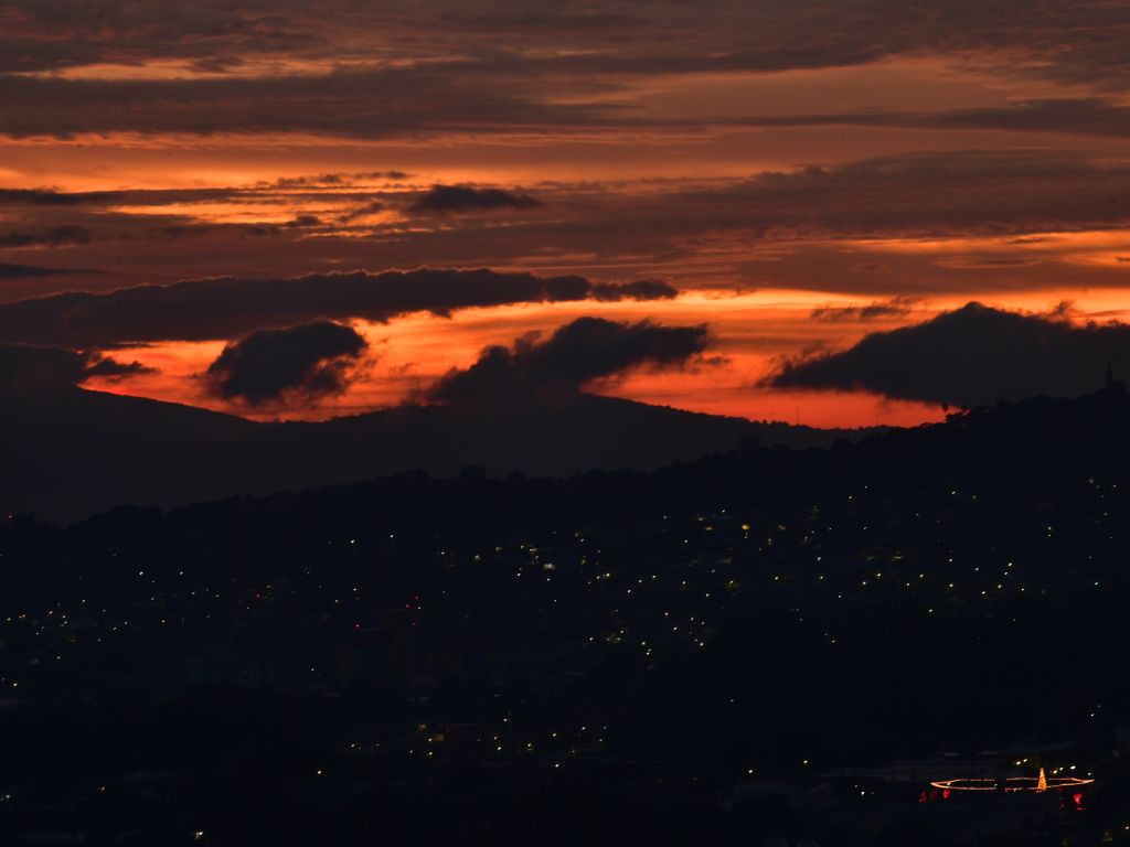 Los intensos tonos anaranjados y las nubes oscuras tiñen el amanecer sobre las siluetas de San Salvador.