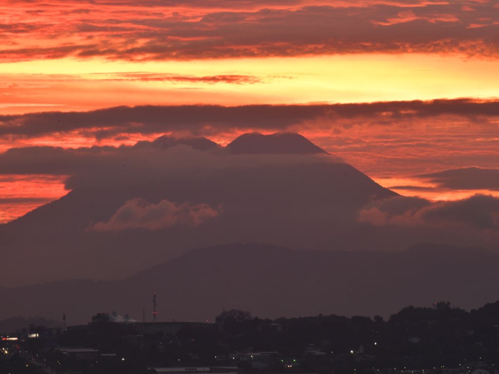La silueta del volcán de San Vicente emerge entre mantos de nubes al despuntar los primeros rayos de luz.