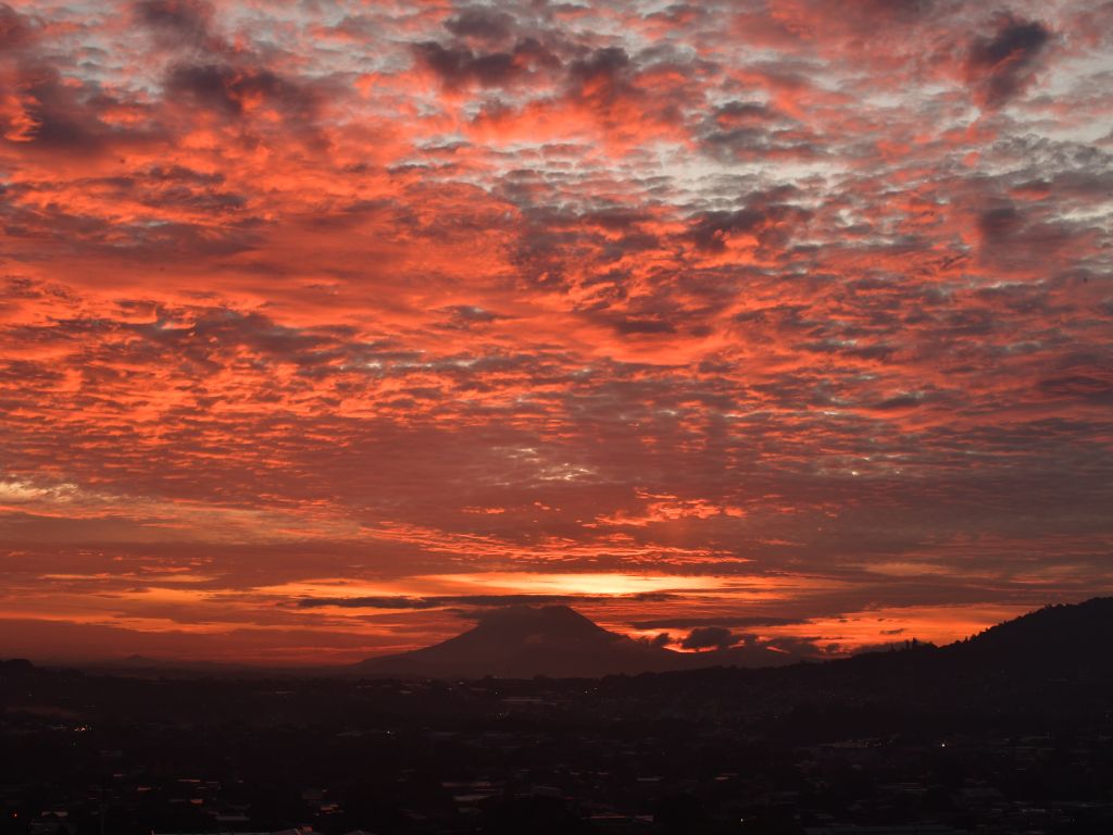 Un mar de nubes abigarradas se enciende en tonos carmesí sobre el horizonte lejano de la ciudad.