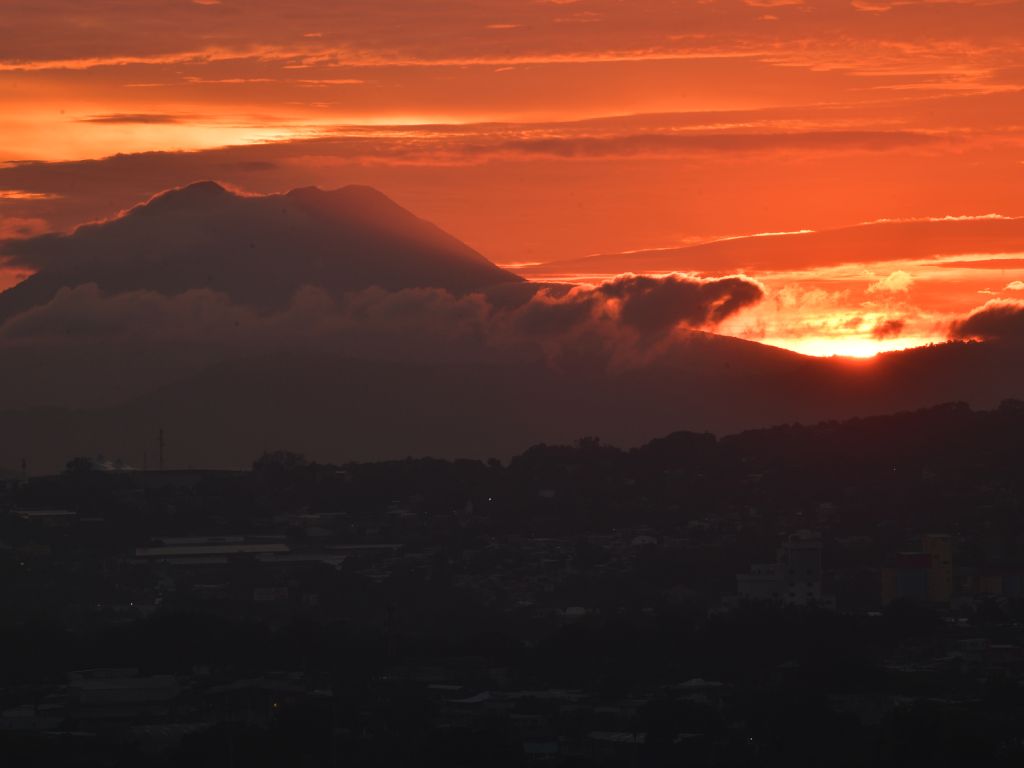 El sol asoma por la montaña inundando el cielo de un rojo ardiente tras las formas del volcán.