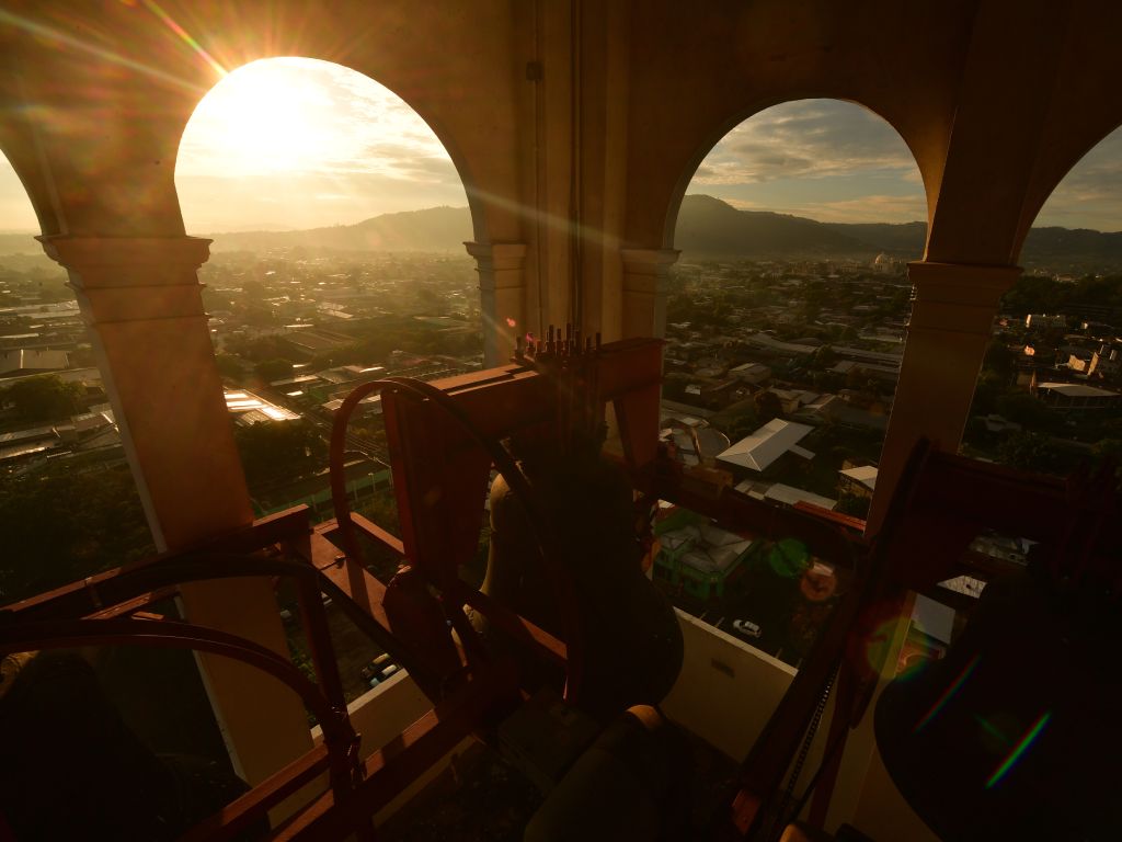 El sol del amanecer se filtra intensamente a través de los arcos, iluminando el horizonte de la ciudad.