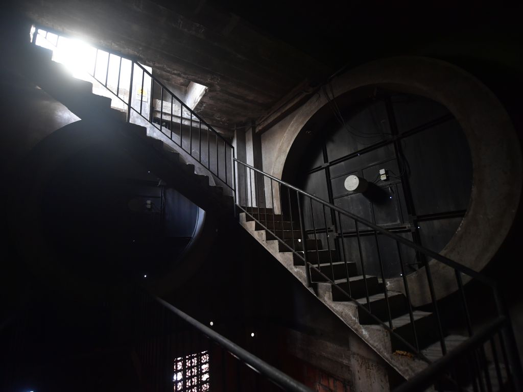 La luz natural penetra en el oscuro interior del reloj del campanario, destacando las líneas geométricas de la escalera de concreto.