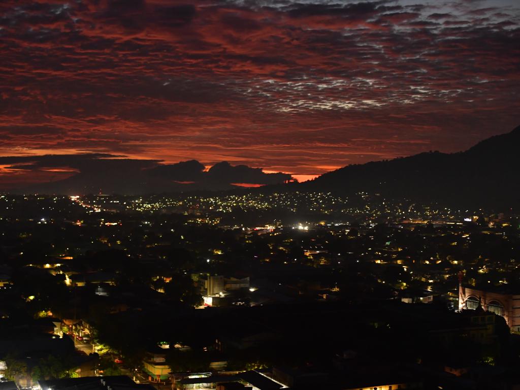 Un impresionante amanecer tiñe el cielo de un rojo intenso sobre las luces de la ciudad que despierta.