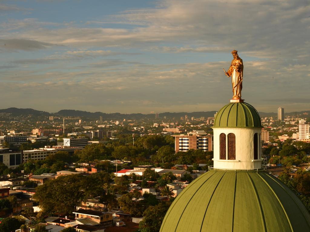 La estatua dorada sobre la cúpula verde brilla intensamente bajo la cálida luz del atardecer.