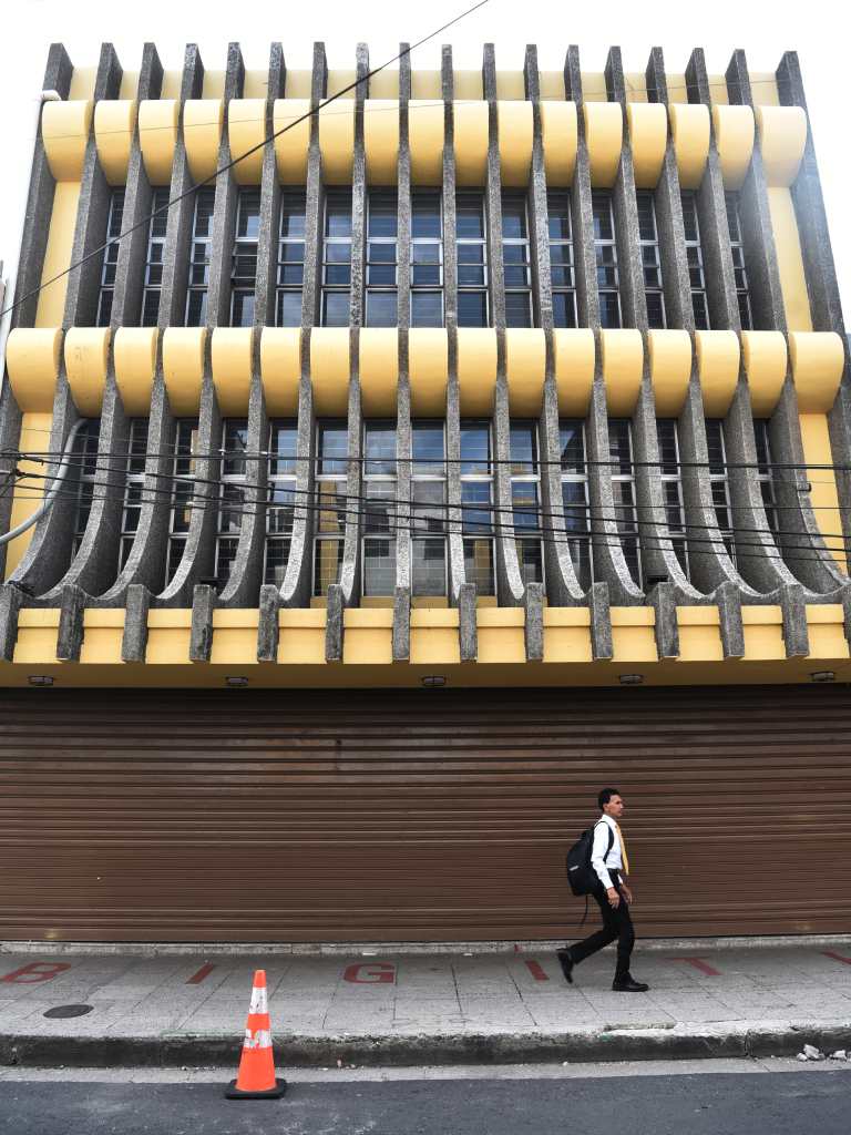 Perspectiva a nivel de calle que resalta la textura del hormigón martillado y los elementos curvos amarillos de la fachada.