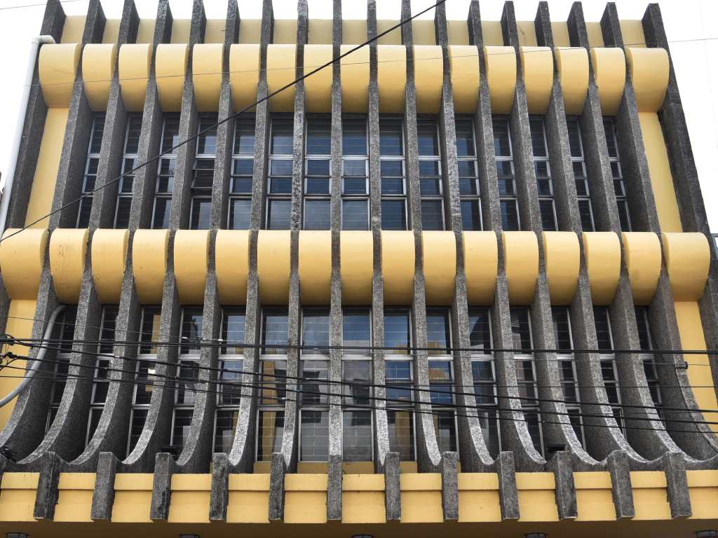 Patrón rítmico de los brise-soleil verticales de hormigón y los elementos de antepecho curvos de color amarillo brillante.
