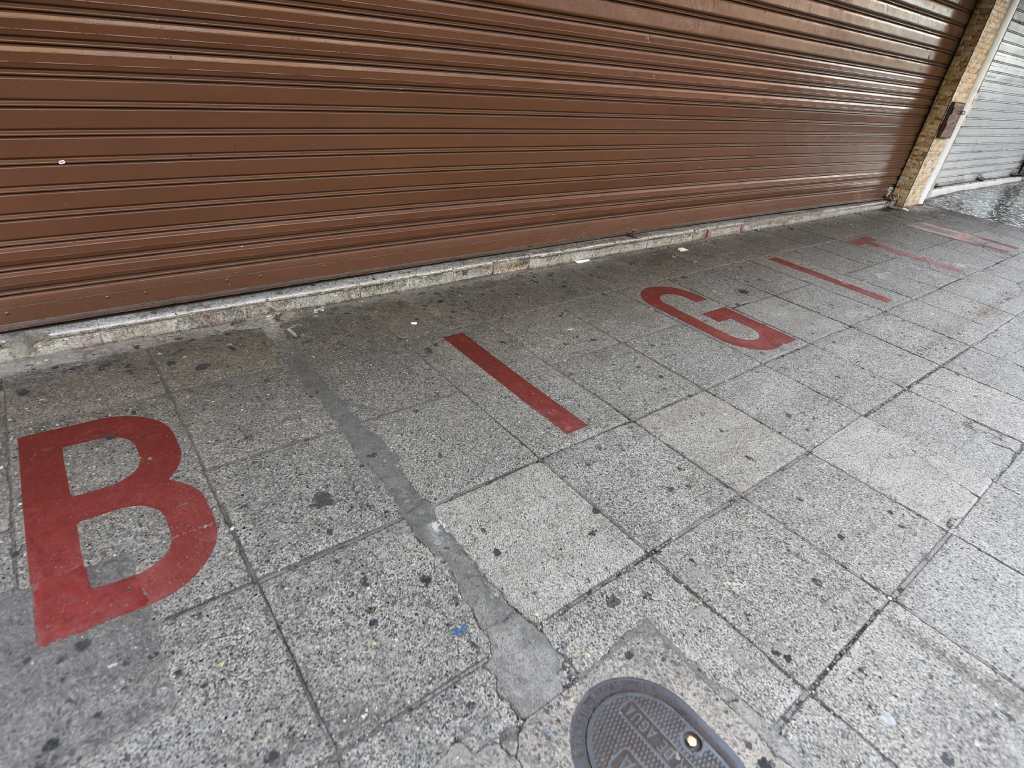Primer plano de las letras "BIGITH" pintadas en la acera de terrazo frente al almacén cerrado.