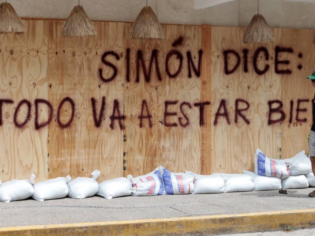 Un hombre pasa junto a un mensaje que dice "Simon dice: todo estará bien", pintado en una cubierta protectora de madera como parte de una campaña optimista ante la llegada del huracán Simón en Puerto Vallarta, estado de Jalisco, México, el 10 de octubre de 2026.