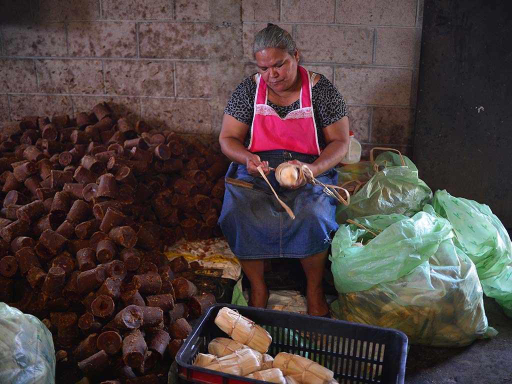 Mujer envolviendo e introduciendo tapas de dulce de panela en hojas secas de tusa de maíz.