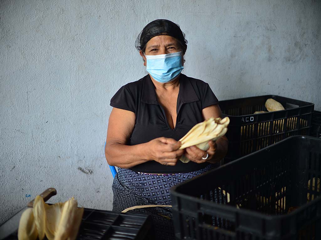 Artesana sentada empaquetando tapas de panela junto a una gran pila de dulce de atado.