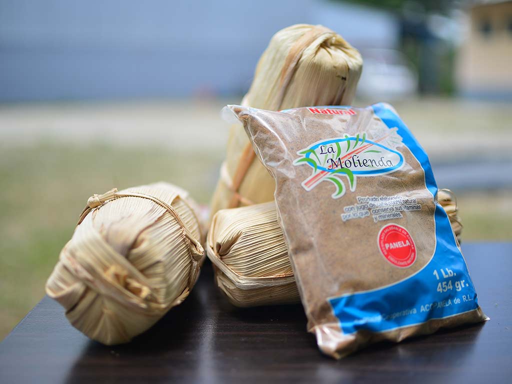 Muestra de atados de dulce envueltos en tusa junto a una bolsa empaquetada de panela granulada.