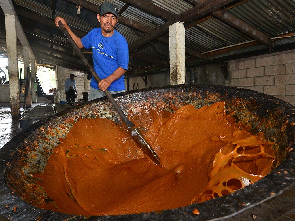 Operario batiendo la densa miel de panela con una paleta de madera en un recipiente metálico.